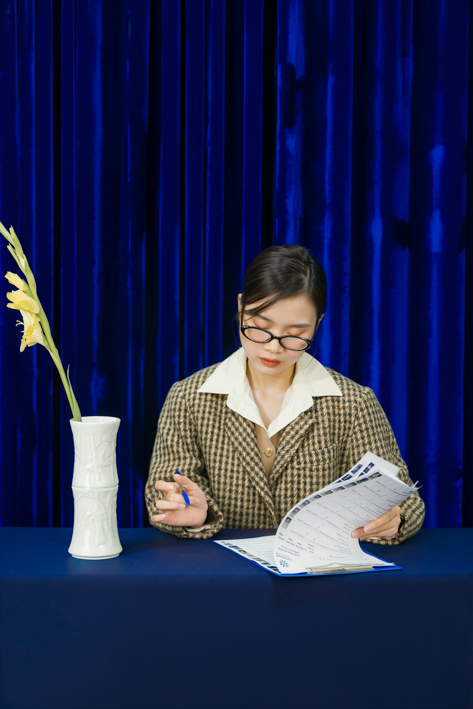 Young woman in glasses reviews documents at a table with flowers.
