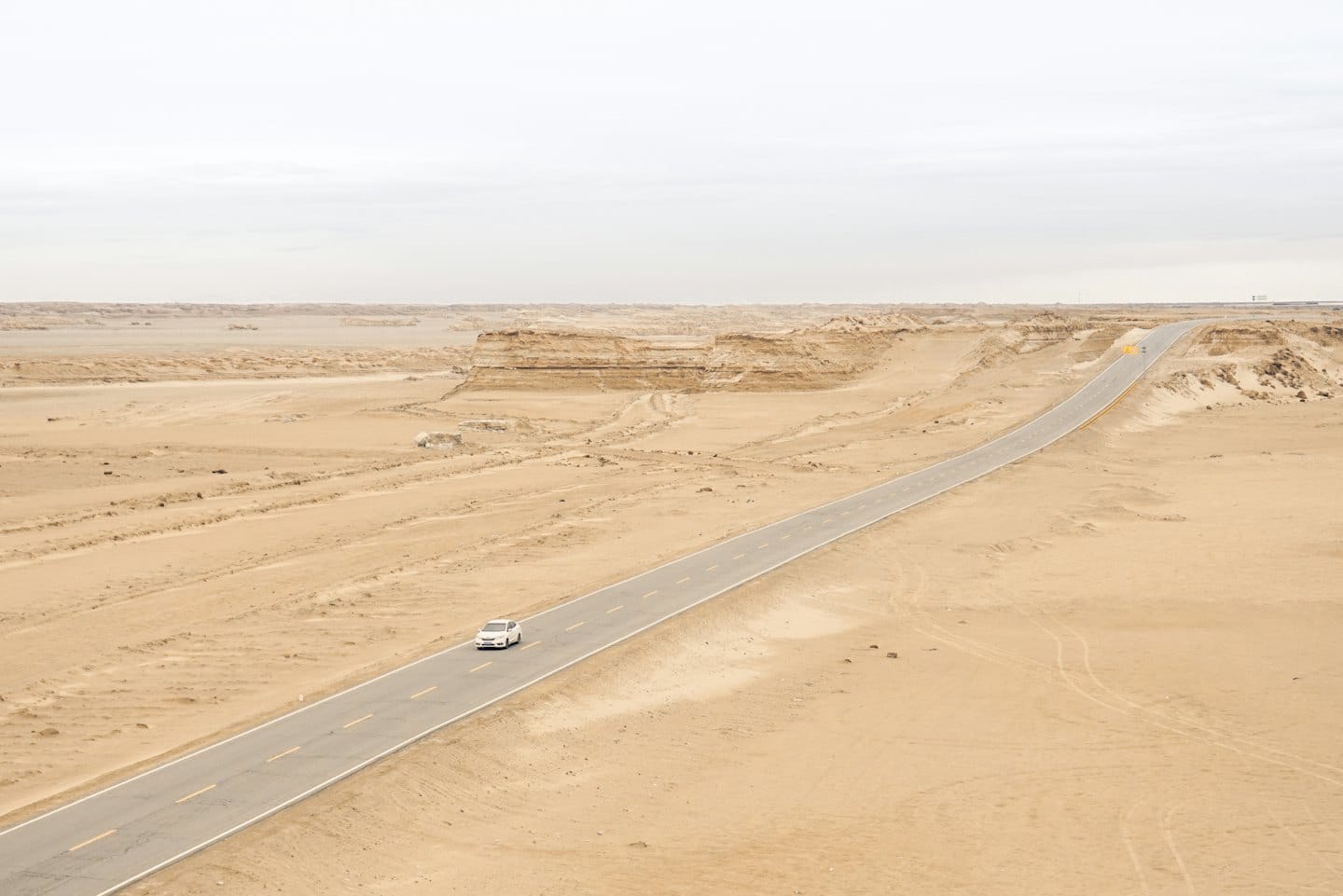 A white car travels along a straight desert highway.