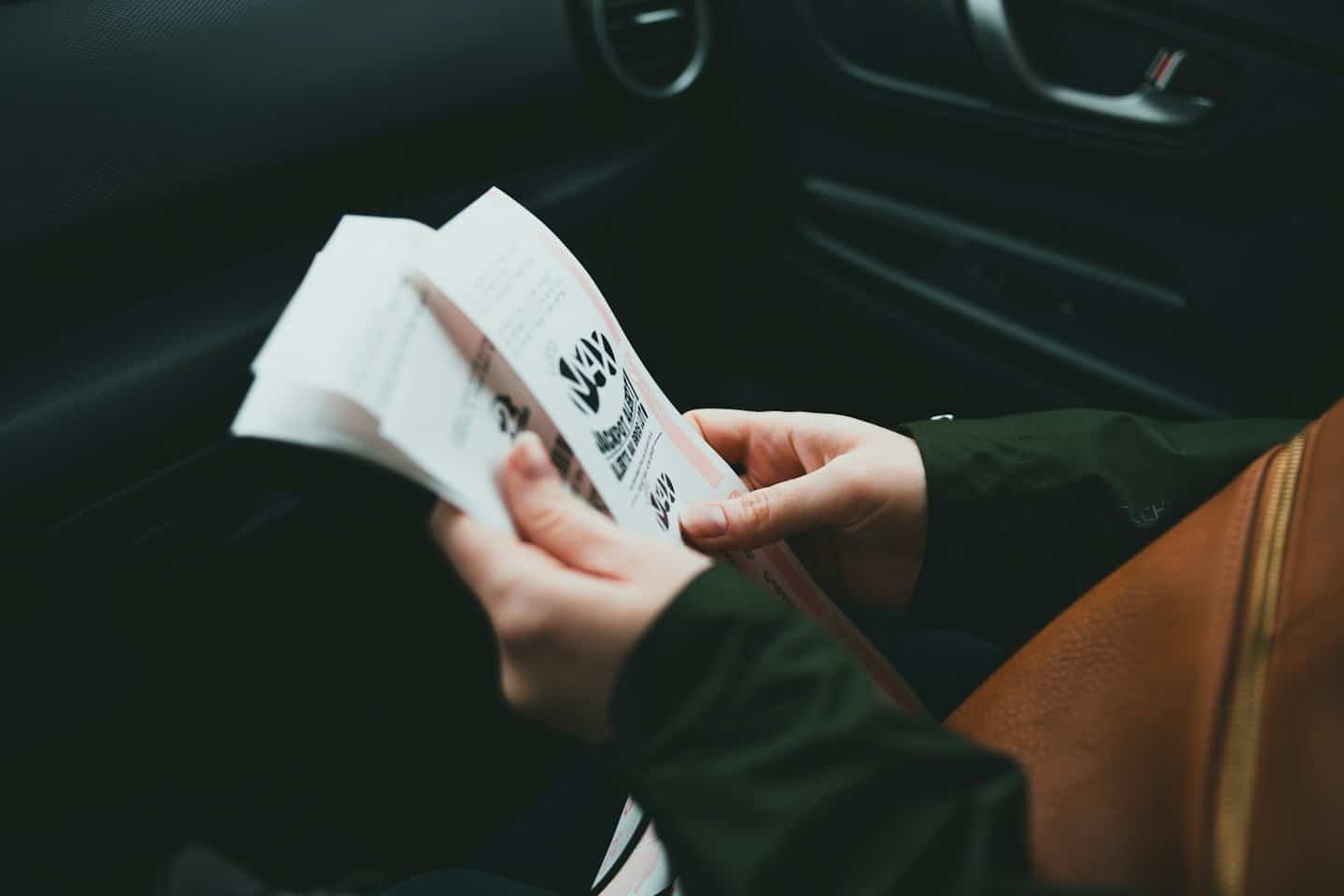 Hands holding paper receipts inside a car.